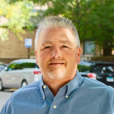 Middle-aged man with spiky grey hair and a goatee wearing a blue button-down shirt.